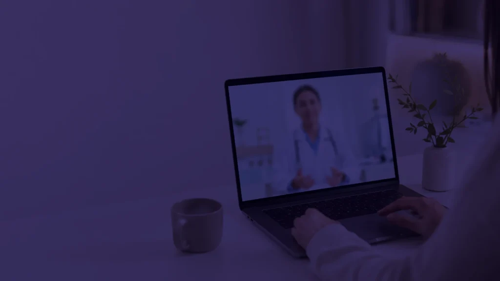 Video-consulta médica en línea abierta en una laptop, con la pantalla como única fuente de luz