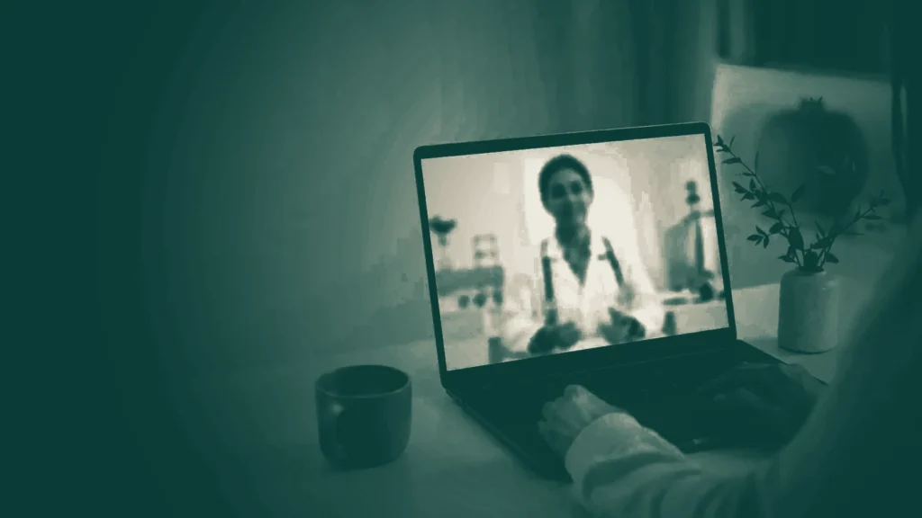 Video-consulta médica en línea abierta en una laptop, con la pantalla como única fuente de luz